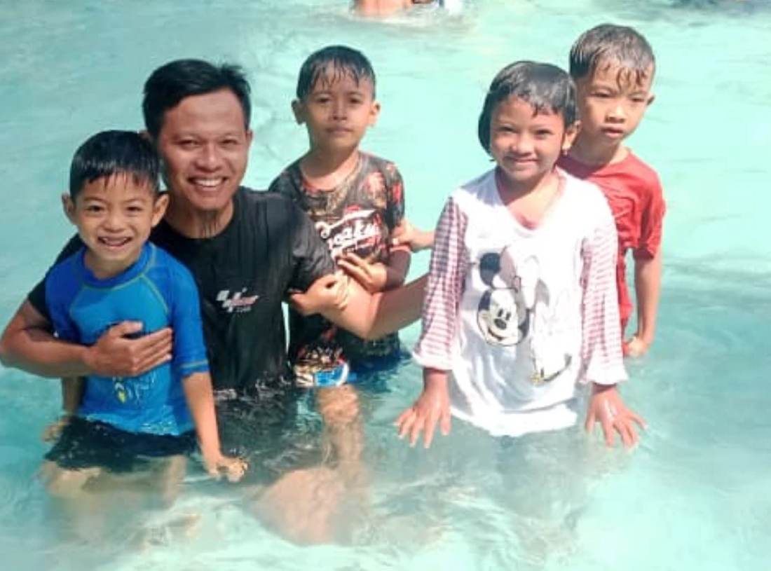 Muhajir laughing in the water with a group of children during a family outing on Lombok.